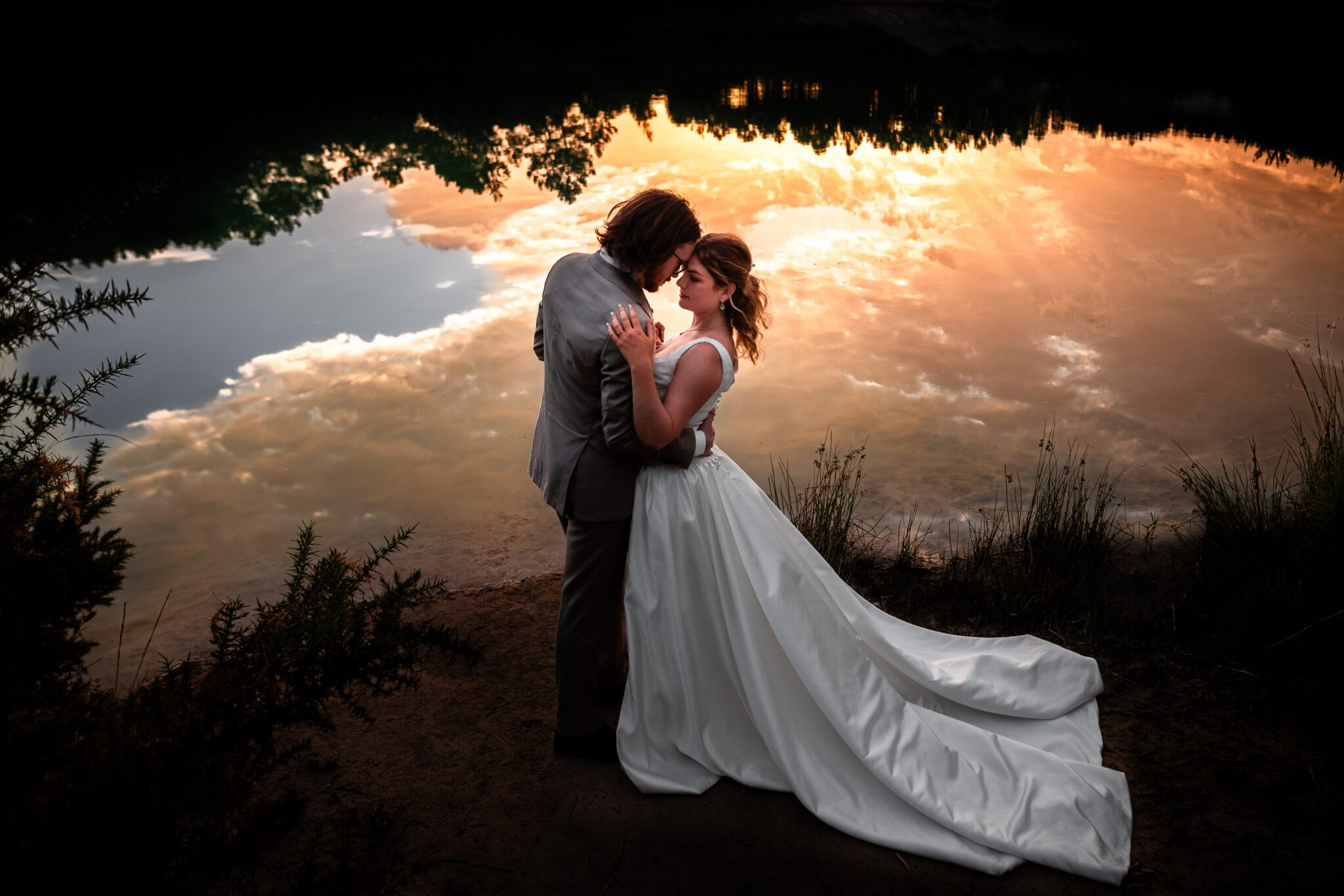Photo épique d'un couple de mariés au bord d'un lac. Le soleil couchant se reflète dans l'eau et le couple est au centre de l'image baigné dans cet univers onirique. Cette photo de mariage a été réalisée par Antoine OLLIER photographe de mariage en Charente