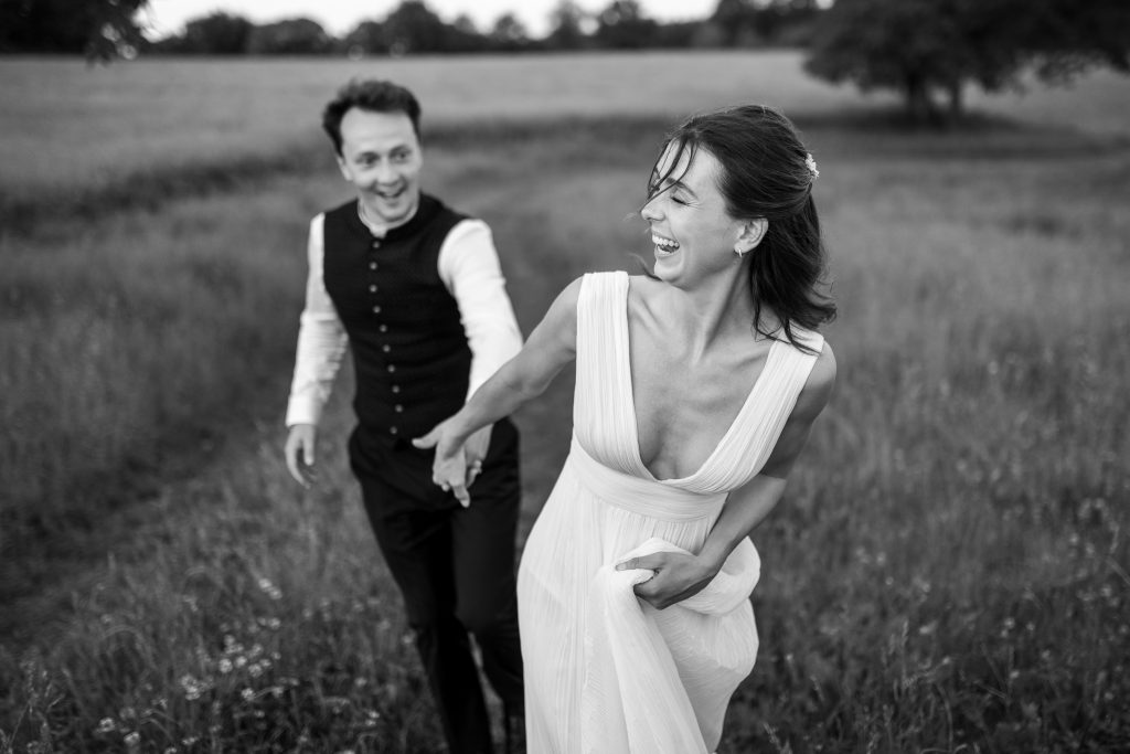 Une photo de couple qui court main dans la main dans un champ en Charente. Une photo réalisée par le photographe de mariage Antoine OLLIER lors de la réalisation des images du couple.